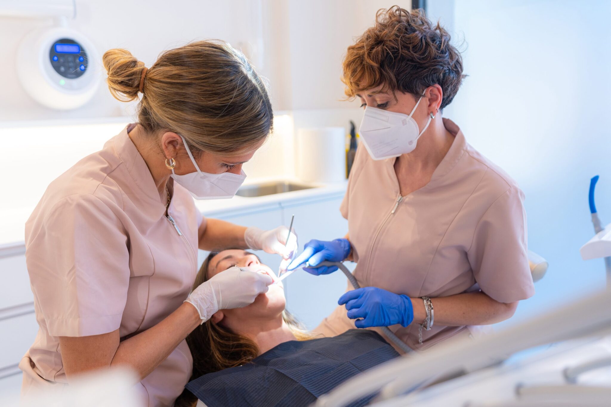 Deux professionnelles dentaires effectuent un soin dentaire sur une patiente en clinique.